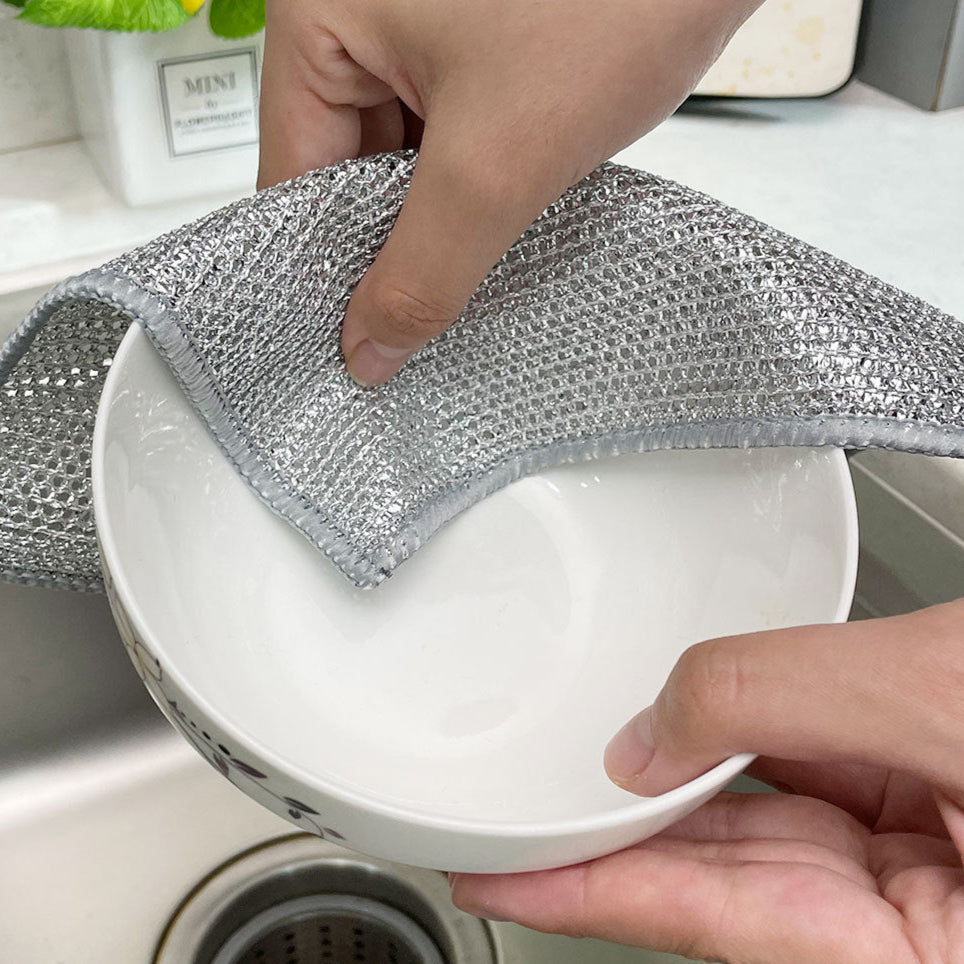 Person cleaning a white bowl with a metallic scrubber in a kitchen setting
